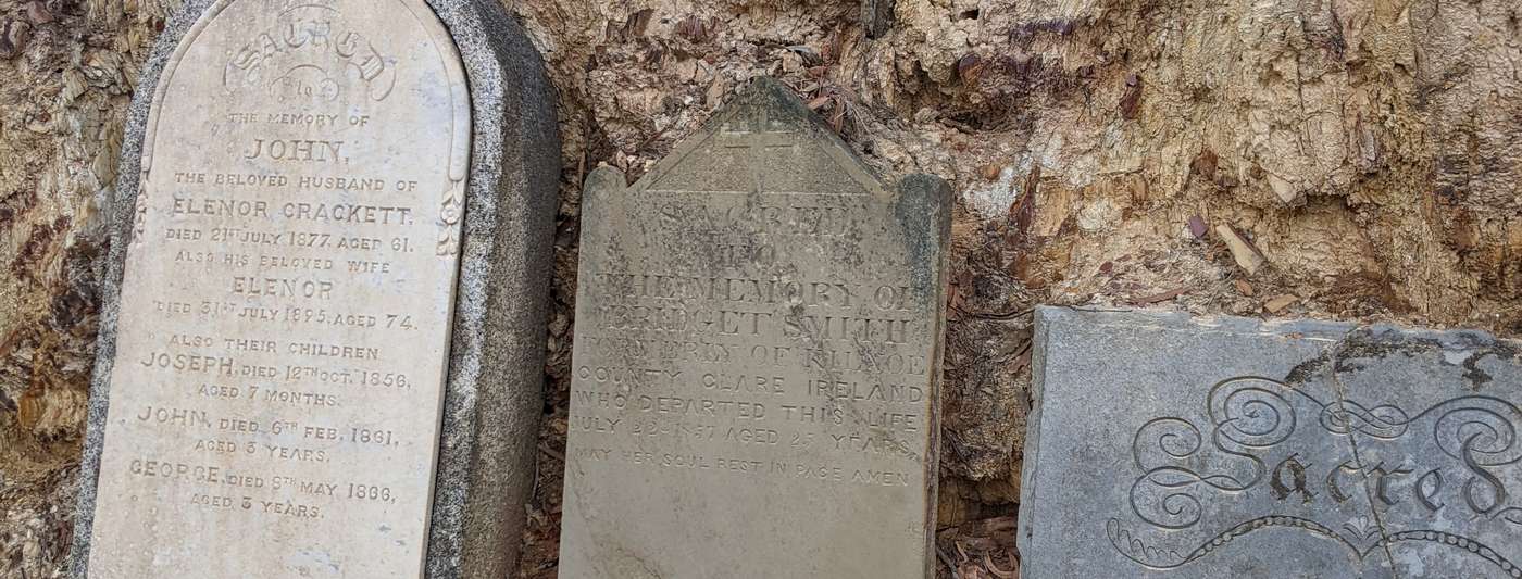 Three weathered headstones from the 1850s-1870s leaning against an eroded embankment at Castlemaine Cemetery.